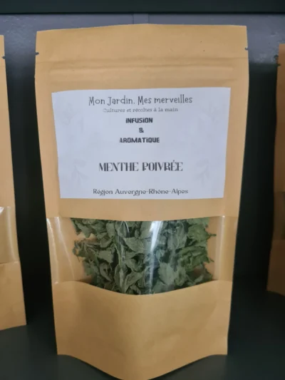 Petit sachet en papier kraft avec une fenêtre transparente laissant apparaître les feuilles de menthe poivrée séchées de couleur verte. Une étiquette blanche indique l'intitulé du produit