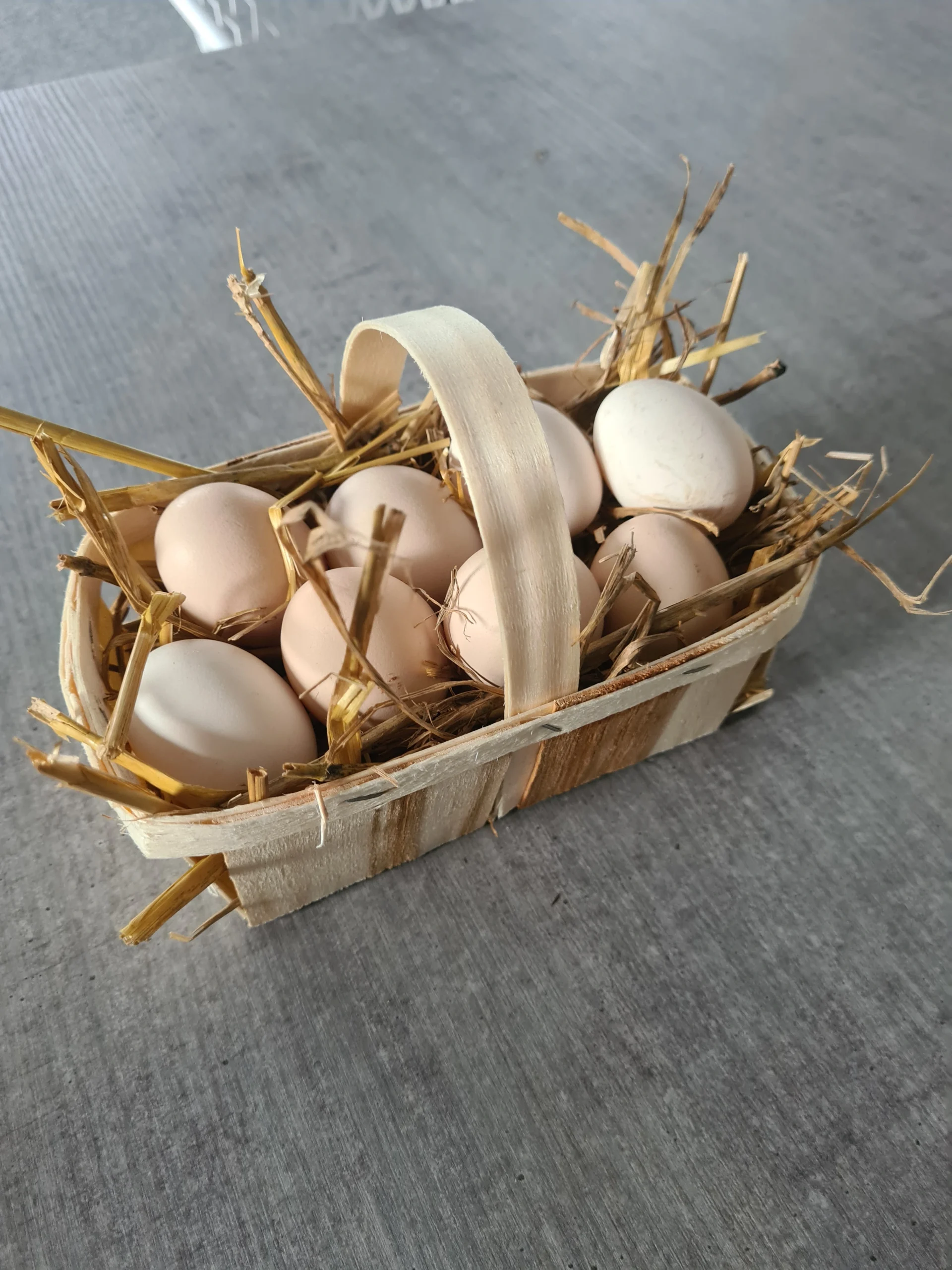 Cette image représente un panier en bois avec du foin et des œufs posés dessus